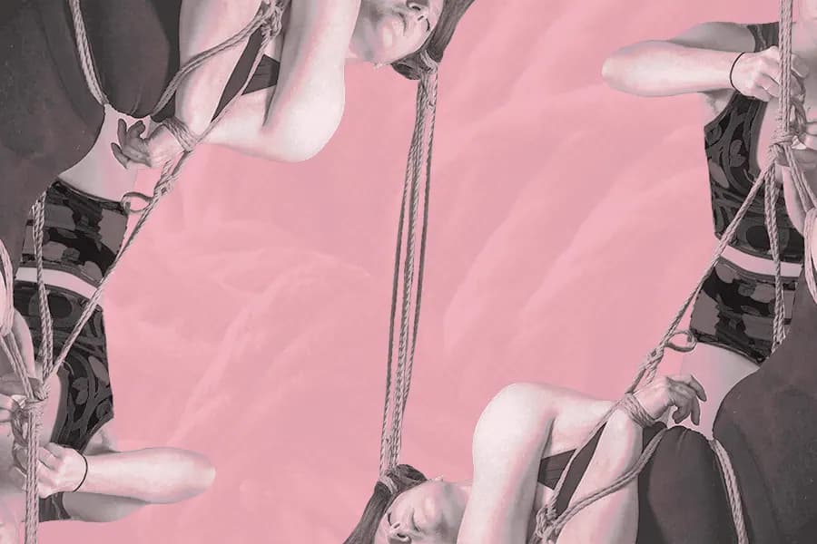 Close-up of hands holding rope around shoulders, lit in blue and magenta tones.