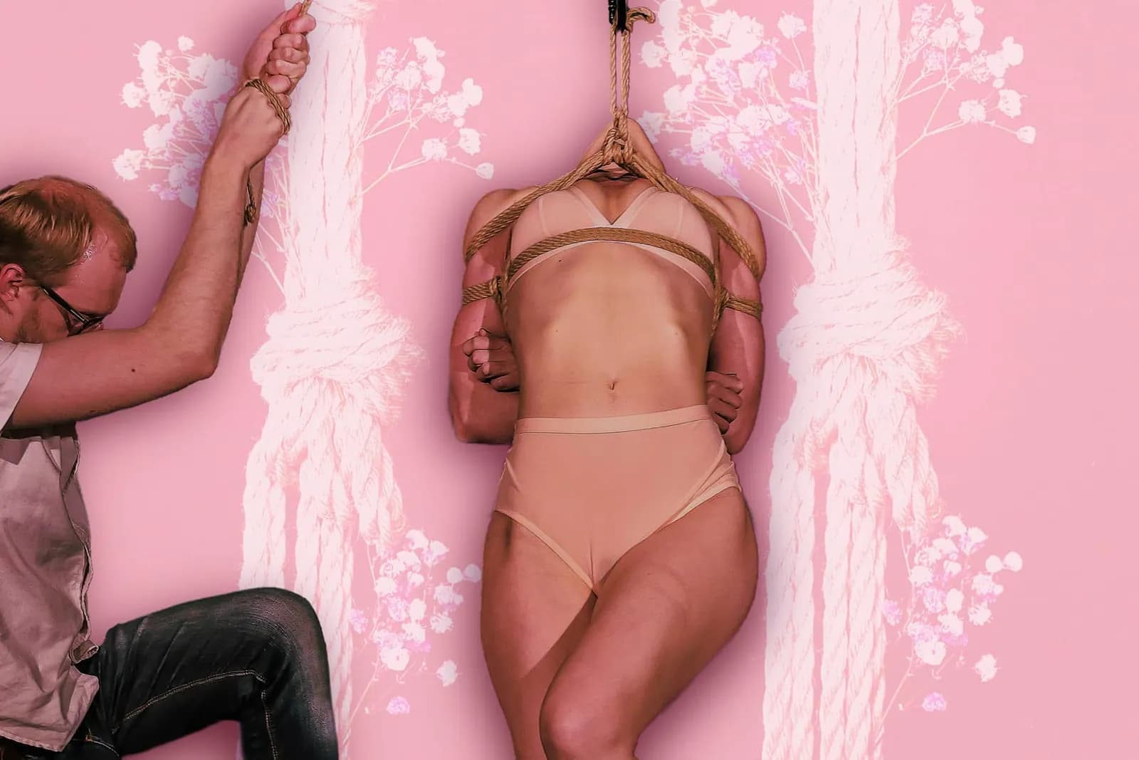 Rigger tying ropes on a suspended model wearing nude lingerie against pink backdrop.