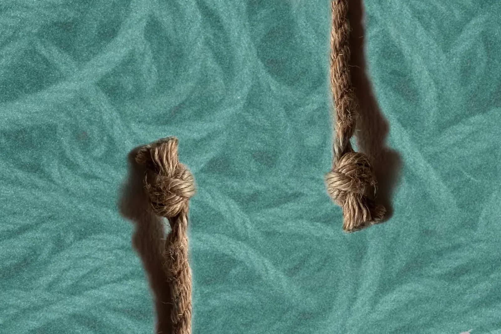 basic shibari knots hanging vertically against a textured teal background with rope and soft shadows