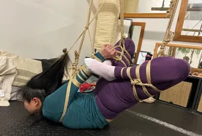 A person suspended upside-down in rope, photographed in black and white.