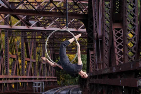 A person suspended upside down in rope harness against industrial metal framework.