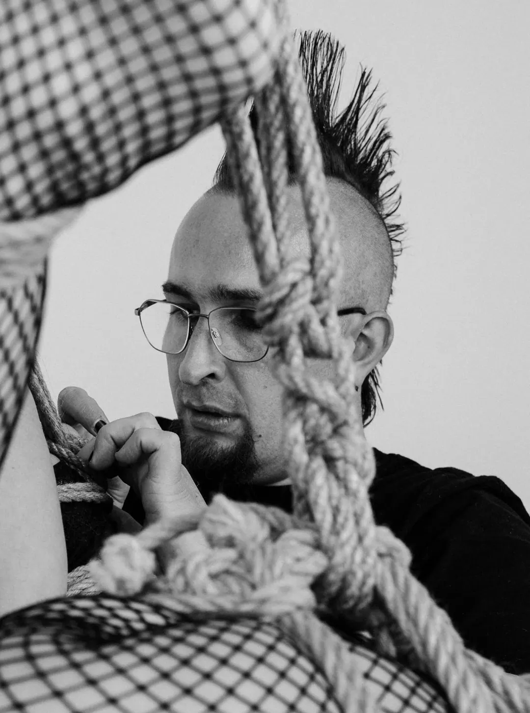 A person examines a length of rope closely in black and white.