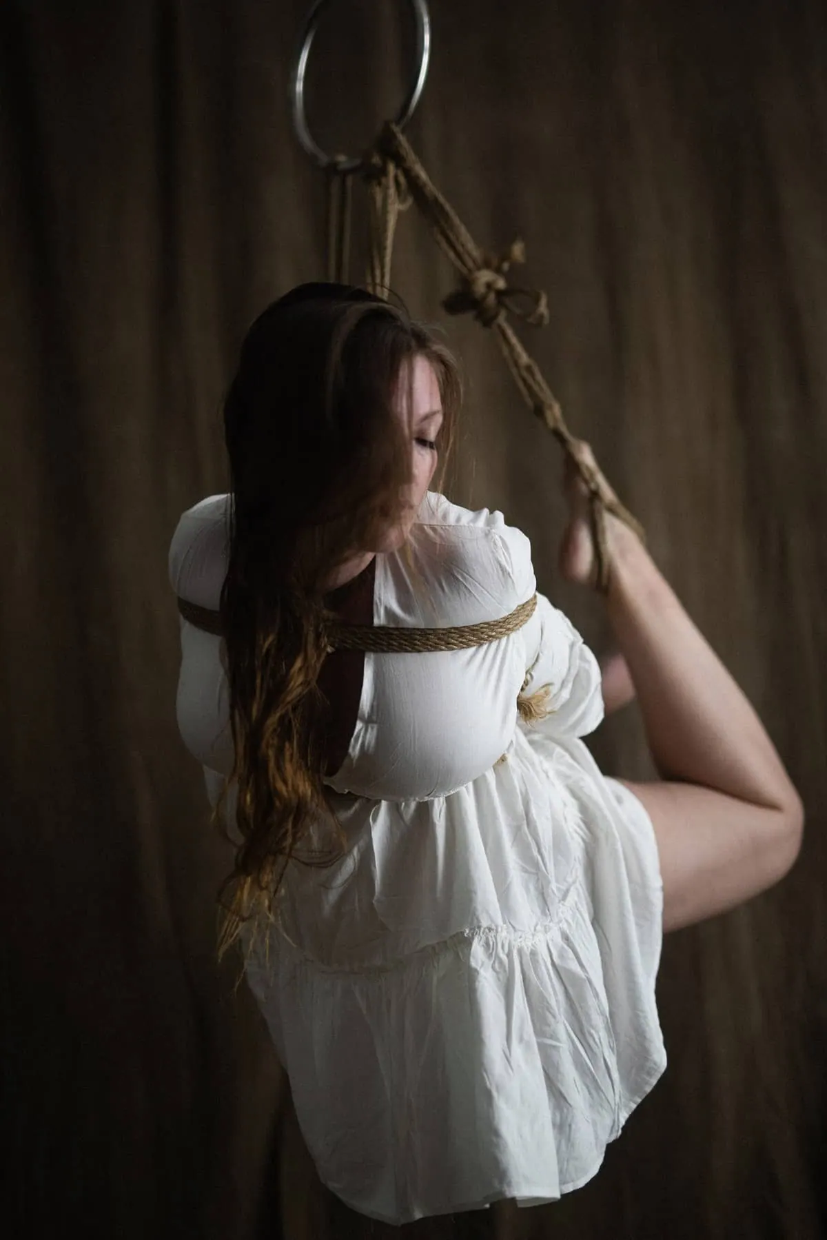 A person suspended horizontally with natural rope.