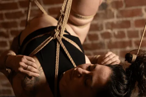 Close-up of a person's chest in a rope harness with hands holding rope strands.