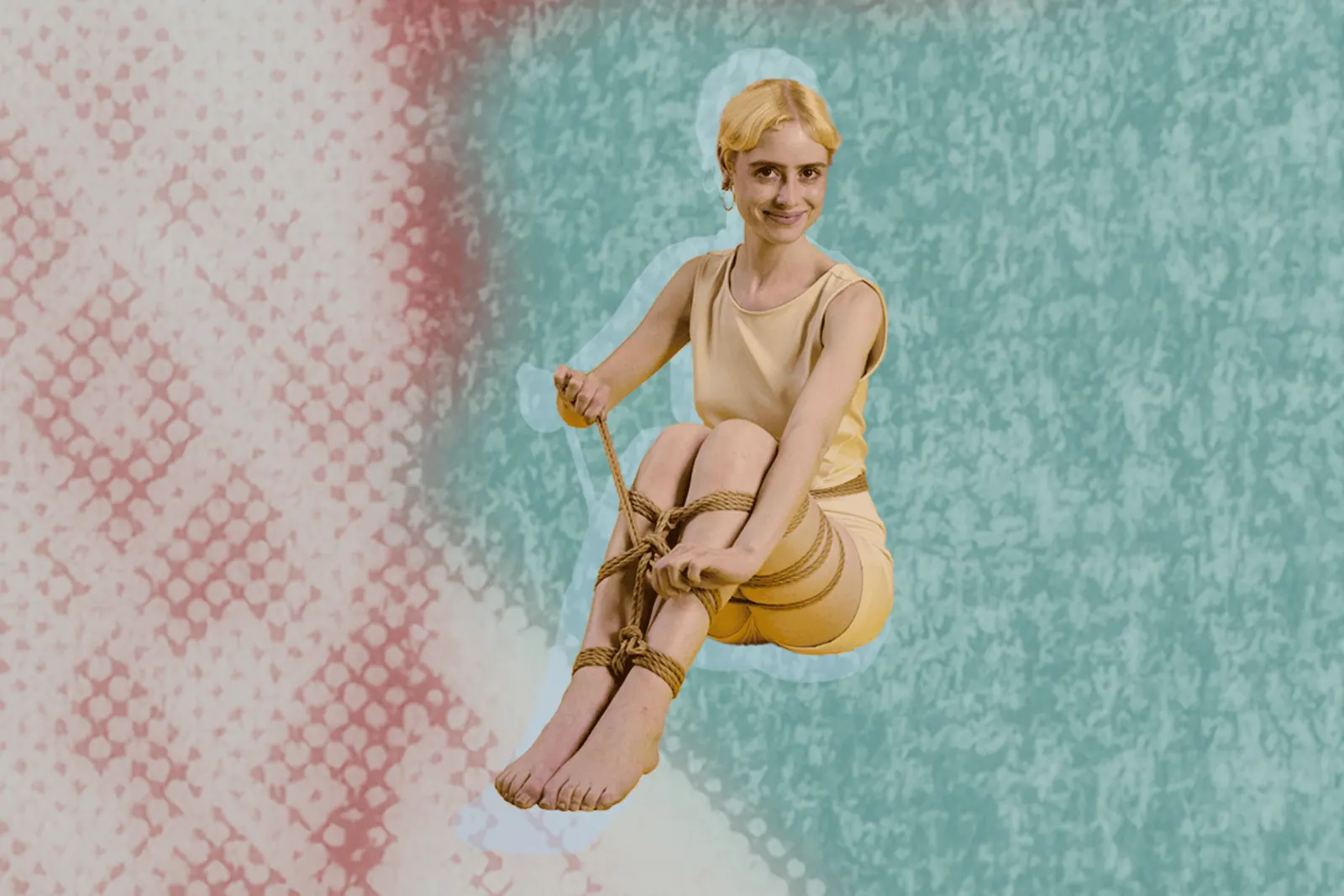 young woman self-tying her legs with a smile on a teal, pink background.