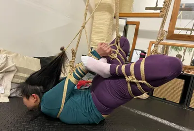 A person suspended upside-down in rope, photographed in black and white.